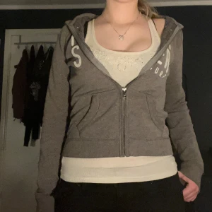 Hollister ziphoodie - Grå hoodie från Hollister med dragkedja. Utmed bröstet sträcker sig Hollister och surf i stora respektive mindre, vita bokstäver. :)   ・❥・Bra skick trots flera tidigare ägare ・❥・Sitter tajt och är i storlek XS ・❥・Inga snören  ・❥・Rätt bra kvalitet (tjockt tyg)  Ställ gärna frågor eller be om fler bilder, samt tryck på Köp nu!