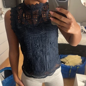 Mörkblå spetsblus - Mörkblå spetsblus med hög hals och detaljerat mönster. Från VINTAGE Stories storlek 34