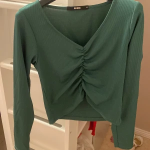 Grön ribbad topp från Bik Bok - Snygg grön ribbad topp från Bik Bok med v-ringning och rynkdetalj framtill. Perfekt för en stilren look.