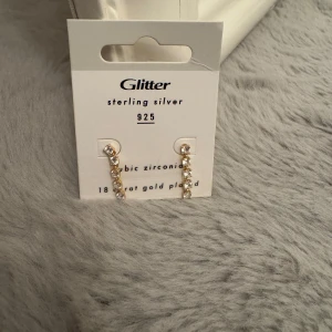 Örhängen guld platerade med cubic zirconia - Snygga örhängen från Glitter i sterling silver 925 med cubic zirconia. De är 18 karat guldpläterade och har en elegant design som passar perfekt för att ge en touch av glamour. Använda bara en gång. Orginalpris: 349kr priset kan diskuteras 🫶🏼