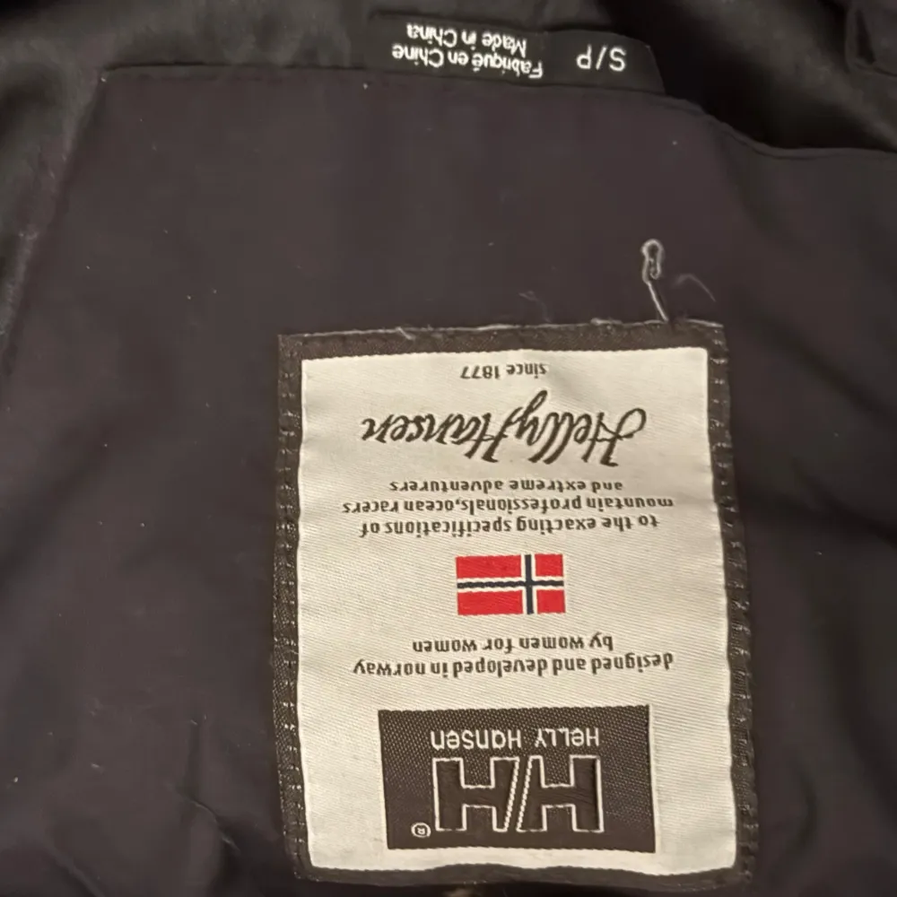 Säljer en svart jacka från Helly Hansen med huva och knappar. Perfekt för kyligare dagar med sin praktiska design och flera fickor. Helly Hansen-logga på bröstet ger en sportig touch.. Takit.