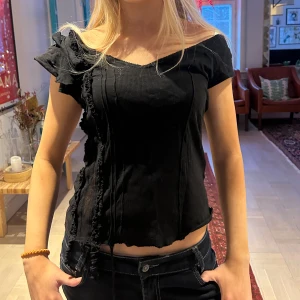 Svart offshoulder topp - Snygg svart offshoulder topp med volangdetaljer. Toppen har en ribbad struktur och en asymmetrisk design som ger en unik look😍😝