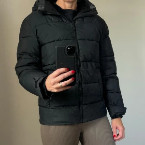 Svart pufferjacka - Säljer en snygg svart pufferjacka som är perfekt för kyliga dagar. Jackan har en dragkedja framtill och långa ärmar. Den är quiltad och ser riktigt varm och gosig ut. Perfekt för vintern!