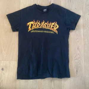 Thrasher t-shirt - Säljer en thrasher t-shirt👕då den inte används. Inte jätte bra skick ett litet hål i den vänstra armhålan och färgen har lossnat lite på baksidan båda syns på bild. Orginal pris 449 SEK💵 va inte blyg och höra av dig vid fler frågor eller bilder😀