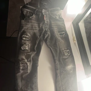 Svarta slitna jeans från Dsquared2 - Säljer ett par svarta/grå jeans från Dsquared2. De har en slim passform och har slitningar+färgstänk fram och bak. Jeansen har 4 knappar framtil för bästa passformen. Riktigt sköna stora fickor. Skick 9/10 - nypris 6500, köpta från farfetch. PM mig