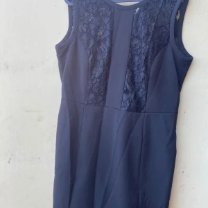 Mörkblå klänning från H&M - Säljer en elegant svart klänning från H&M. Den är ärmlös med vackra spetsdetaljer på framsidan och baksidan. Klänningen har en dragkedja i ryggen för enkel påklädning. Perfekt för festliga tillfällen!