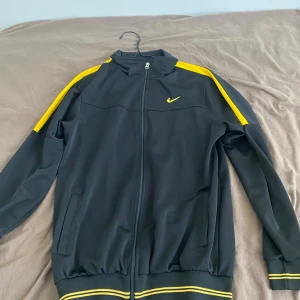 Svarta träningsbyxor från Nike - Säljer ett par svarta träningsbyxor från Nike med gul detalj. Byxorna har en elastisk midja och är perfekta för träning eller en avslappnad dag. De har en normal passform och är gjorda i ett bekvämt material.