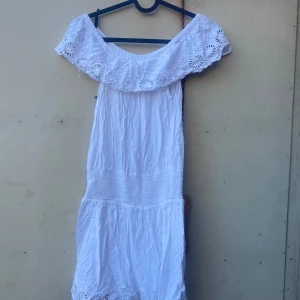 Vit offshoulder klänning - Säljer en superfin vit offshoulder klänning med vackra spetsdetaljer. Perfekt för sommarens alla fester eller en dag på stranden. Klänningen har en luftig passform och är gjord i ett lätt material som känns skönt mot huden. Passar perfekt för en 11-åring!