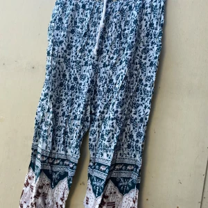 Mönstrade byxor med blommigt motiv - Säljer ett par lösa och bekväma byxor med ett snyggt blommigt mönster i blått och vitt. Byxorna har en elastisk midja med snörning för extra komfort. Perfekta för en avslappnad sommarlook! Skulle säga att det är storlek S