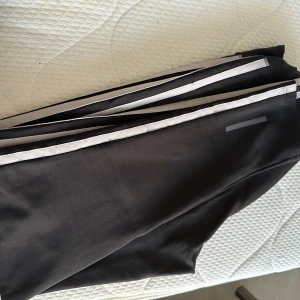 Svarta träningsleggings med reflexdetaljer - Säljer ett par svarta träningsleggings i storlek M. De har snygga reflexdetaljer längs sidorna som gör dem perfekta för kvällspromenader eller löprundor. Materialet är stretchigt och bekvämt, vilket ger en bra passform under träning. Perfekta för dig som vill ha både stil och funktion!