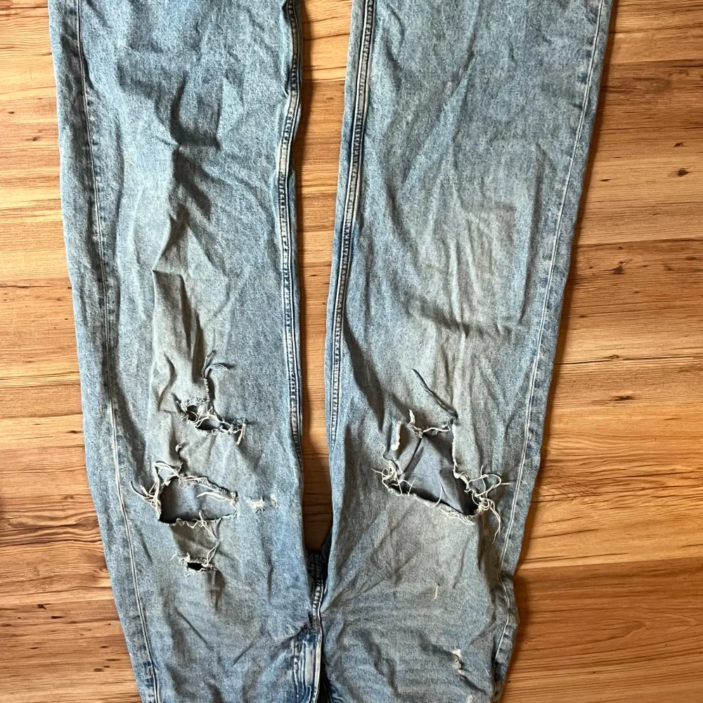 Säljer ett par blå jeans med slitningar på knäna. De har en hög midja och en straight passform. Perfekta för en avslappnad och trendig look!. Jeans & Byxor.