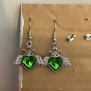 Gröna hjärtformade örhängen med strass - Säljer ett par superfina örhängen med gröna hjärtformade stenar. De har en glittrig strassdetalj runt hjärtat och är i silverfärg. Perfekta för att liva upp vilken outfit som helst!