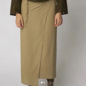 Beige omlottkjol - Snygg beige omlottkjol i ett mjukt material. Kjolen har en knytning i midjan och en elegant omlottdesign som ger en stilren look. Perfekt för både vardag och mer uppklädda tillfällen.