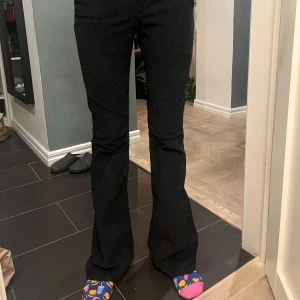 Svarta bootcut jeans - Snygga svarta bootcut jeans med låg midja. Perfekta för en stilren look. De har klassisk femficksdesign och knappar i silverfärg. Passar utmärkt till både vardag och mer uppklädda tillfällen.