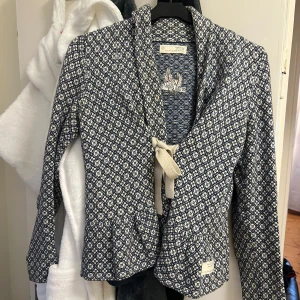 Mönstrad jacka från Odd Molly - Snygg mönstrad jacka från Odd Molly i blått och vitt. Jackan har långa ärmar och en knytning framtill. Perfekt för att ge din outfit en unik touch. Storlek 0 så Xs