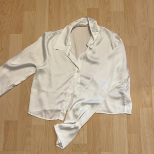 Vit satinblus från Pull&Bear - Elegant vit blus i satin från Pull&Bear. Blusen har långa ärmar och knappar framtill, perfekt för en stilren look. Den mjuka satinfinishen ger en lyxig känsla.