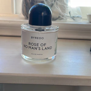 Rose of No Man's Land Eau de Parfum från Byredo - Säljer en parfymflaska från Byredo, 'Rose of No Man's Land'. Flaskan är genomskinlig med en svart rund kork och rymmer 100 ml. Doften är känd för sina blommiga och fräscha toner, perfekt för den som älskar en sofistikerad och modern parfym.