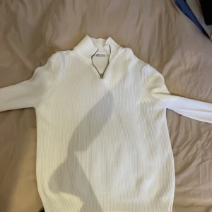 Vit half zip från Zara - Säljer en stilren vit ribbad tröja från Zara med dragkedja vid halsen. Perfekt för kyligare dagar med sin långa ärmar och bekväma passform. Enkelt att matcha med olika outfits.