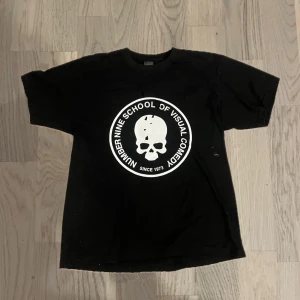 Number Nine ‘School Of Visual Comedy’ Tshirt - Cool svart t-shirt från Number (N)ine med ett stort vitt dödskalletryck och texten 'School of Visual Comedy'. Perfekt för en edgy look.