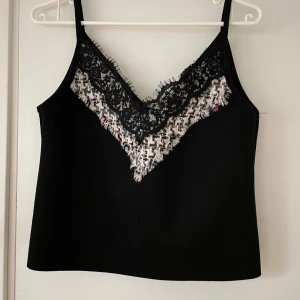 Svart linne med spetsdetaljer från Zara - Snyggt svart linne från Zara med spetsdetaljer och ett mönstrat parti i vitt och flerfärgat vid halsringningen. Perfekt för en stilren look.