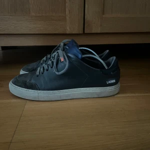 Svarta sneakers med snörning - Säljer ett par svarta sneakers med snörning och vit sula. Skorna har en diskret design med texten '1.40MM' på sidan. Perfekta för en avslappnad stil.