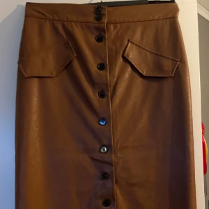 Kjol i fuskskinn  - Cool lång kjol i fuskskinn med knappar hela vägen på framsidan. Skönt foder på insidan. Fickorna är även de fusk 😉, går alltså inte att öppna. Knapparna går att öppna upp hela vägen så man kan öppna som sprund. Storlek 44, kjolen är från H&M. 