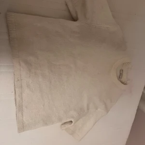 Beige stickad tröja från Gina Tricot - Mysig beige stickad tröja från Gina Tricot i premiumkvalitet. Tröjan har korta ärmar och ribbade kanter vid ärmslut och nederkant. Perfekt för en stilren och bekväm look.