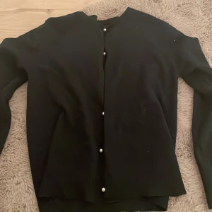 Svart kofta från Zara - Säljer en stilren svart kofta från Zara Knitwear med pärlknappar. Perfekt för kyligare dagar och enkel att matcha med olika outfits. Koftan har långa ärmar och ribbade kanter. 50kr + frakt