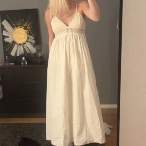 Vit långklänning från Zara - Säljer en vacker vit långklänning från Zara med smala axelband och v-ringning. Klänningen har fina spetsdetaljer och en knytning framtill. Perfekt för sommarens alla tillfällen. Knappt använd💗
