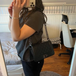 Svart quiltad axelväska - Snygg svart quiltad axelväska med kedjerem och stilren design. Väskan har en praktisk storlek och en elegant look. Köpt på Nelly!