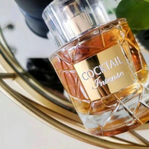 Cocktail Intense Parfym - Elegant parfymflaska med ett unikt rutmönster och gyllene detaljer. Doften 'Intense' ger en lyxig känsla. Flaskan är genomskinlig med en gyllene vätska och har en stilren, transparent kork. Perfekt för den som vill ha en sofistikerad doftupplevelse.