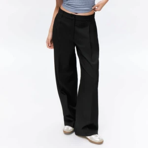 Svarta kostymbyxor - Snygga svarta kostymbyxor med hög midja och vida ben. Byxorna har en klassisk design med knäppning fram och pressveck. Helt oanvända! 