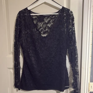 Svart spetstopp  - Svart spetstopp från Gina Tricot med v-ringning och långa ärmar. Perfekt för en stilren look med vackert spetsmönster som ger en sofistikerad touch. Storlek L men sitter som S-M