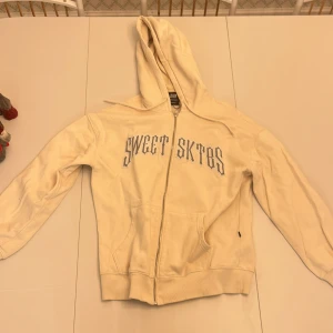 Vit/beige hoodie från Sweet SKTBS - Säljer en beige/vit hoodie från Sweet SKTBS med dragkedja och text på framsidan. Skriv om ni har frågor