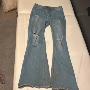 Blå bootcut jeans med slitningar - Säljer ett par blå bootcut jeans med coola slitningar. De har en hög midja och en avslappnad passform som ger en retro känsla. Perfekta för en trendig look!