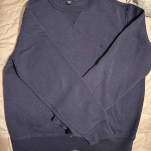 Mörkblå tröja från Ralph Lauren M  10-12 år  - Säljer en stilren mörkblå tröja från Ralph Lauren. Tröjan har långa ärmar och en klassisk rund halsringning. Perfekt för en avslappnad och snygg look. Fint skick 