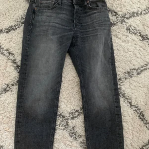 Jack and Jones jeans - Snygga grå jeans med en klassisk femficksdesign och lätt slitna detaljer. Perfekta för en avslappnad stil. De har en dragkedja och knapp framtill. I märket Jack and jones och modellen heter Tapered/Mike.