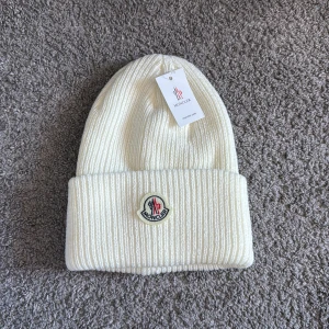 Vit ribbad mössa från Moncler - Snygg vit ribbad mössa från Moncler med broderad logotyp framtill. Perfekt för att hålla värmen under kyliga dagar. Stilren design som passar till det mesta.kom jätte gärna med prisförslag. Aldrig använd. 