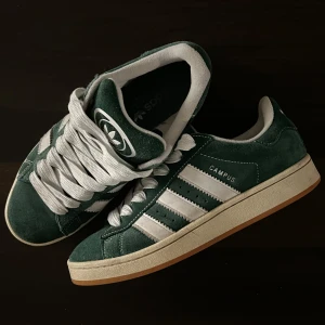 Gröna Adidas Campus sneakers - Snygga gröna Adidas Campus sneakers med vita detaljer och snörning. Skorna har en klassisk design med tre ränder på sidan och en bekväm gummisula. Inga synliga tecken på användning!