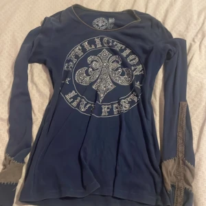 Mörkblå långärmad tröja från Affliction - Säljer en mörkblå långärmad tröja från Affliction med ett stort tryck och dekorativa detaljer på framsidan. Tröjan har en rund hals och kontrasterande sömmar vid ärmsluten. 