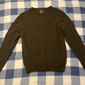 Mörkgrön ulltröja från Oscar Jacobson - Säljer en stilren mörkgrön tröja från Oscar Jacobson, tillverkad i Italien. Tröjan är i ull och har en klassisk rund halsringning med långa ärmar. Perfekt för kyligare dagar.passar bra runt 160cm till 165cm