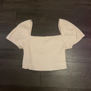 Beige ribbad topp från HM  - Säljer en stilren beige ribbad topp med korta ärmar och en fyrkantig halsringning. Perfekt för en avslappnad look.