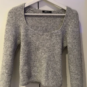Grå stickad tröja från Gina Tricot - Säljer en stilren grå stickad tröja från Gina Tricot. Tröjan har en v-ringad hals och långa ärmar, perfekt för kyligare dagar. Den ribbade strukturen ger en snygg och bekväm passform.