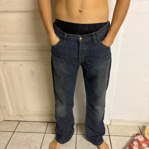 Mörkblå jeans från Lee - Säljer ett par mörkblå jeans från Lee med klassisk femficksdesign och knappgylf. Jeansen har en rak passform och är perfekta för en avslappnad stil. Märkeslogga på bakfickan ger en snygg detalj.