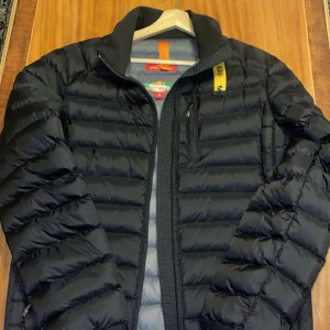 Parajumper jacka  - Snygg svart dunjacka från Parajumpers med dragkedja och hög krage. Jackan har en praktisk bröstficka med dragkedja och är perfekt för kyligare väder. Den quiltade designen ger både stil och värme.