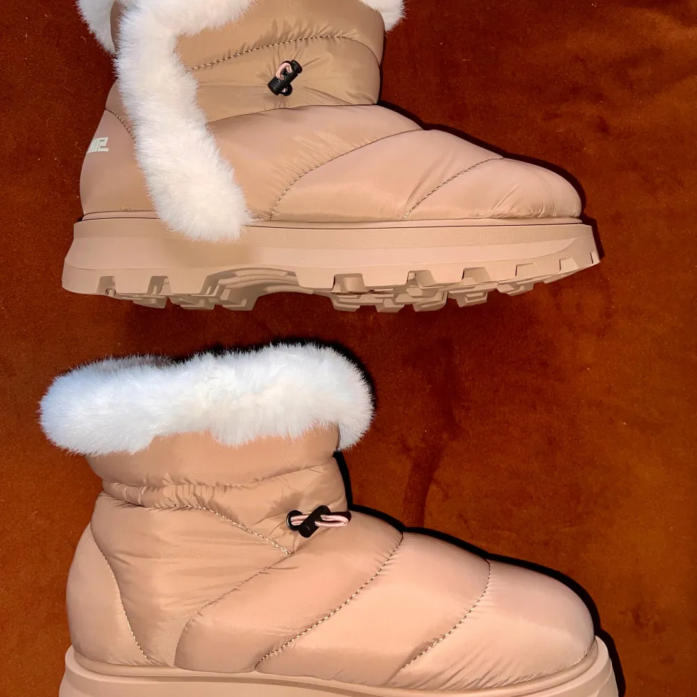 Snygga och varma beige vinterboots med vit pälsdetalj runt kanten. De har en robust sula för bra grepp och en praktisk snörning för justerbar passform. Perfekta för kalla vinterdagar.. Kengät.