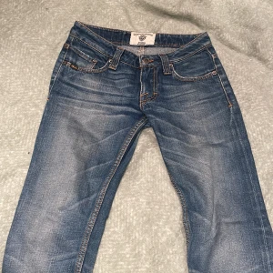 Blå jeans från Tiger of Sweden - Snygga blå jeans från Tiger of Sweden med klassisk femficksdesign och orange sömmar. Perfekta för en avslappnad stil. De har en knappgylf och bälteshällor. Inte så strechiga i tyget och raka i benen.