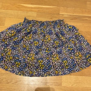 Blommig kjol från H&M - Söt blommig kjol från H&M i en mix av blå, gul och rosa färger. Kjolen har en elastisk midja och volangdetaljer som ger en lekfull look. Perfekt för varmare dagar!