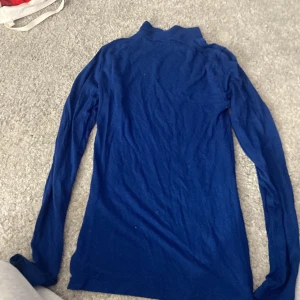 Blå polotröja från Gina Tricot - Säljer en stilren blå polotröja från Gina Tricot. Tröjan har långa ärmar och är perfekt för kyligare dagar. Den är gjord i ett mjukt material som känns skönt mot huden.