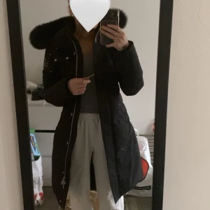 Vinterjacka  - Snygg svart parkajacka från Moose Knuckles med pälsdetaljer på huvan. Jackan har dragkedja och knappar framtill samt flera praktiska fickor. Perfekt för kyliga dagar.